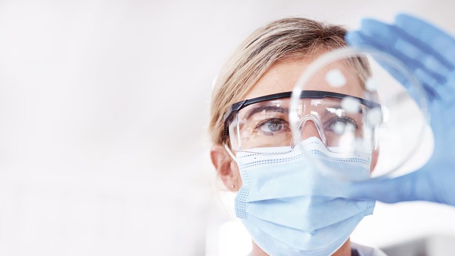 Frau mit Schutzbrille und Maske hält eine Petrischale in einer Apotheke für sichere Krebstherapie.