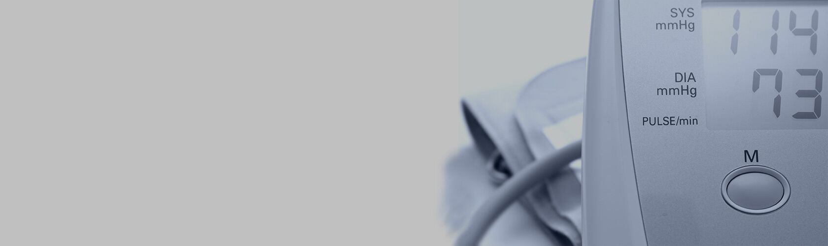 Digitales Blutdruckmessgerät mit Anzeige von 114/73 mmHg und Pulsmessung neben Manschette.
