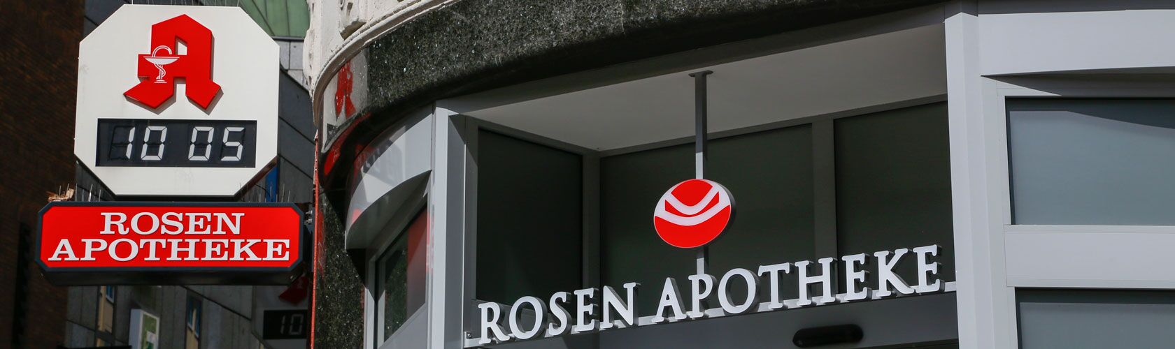 Fassade der Rosen Apotheke mit Uhr und Notdienst-Schild bei Tageslicht.